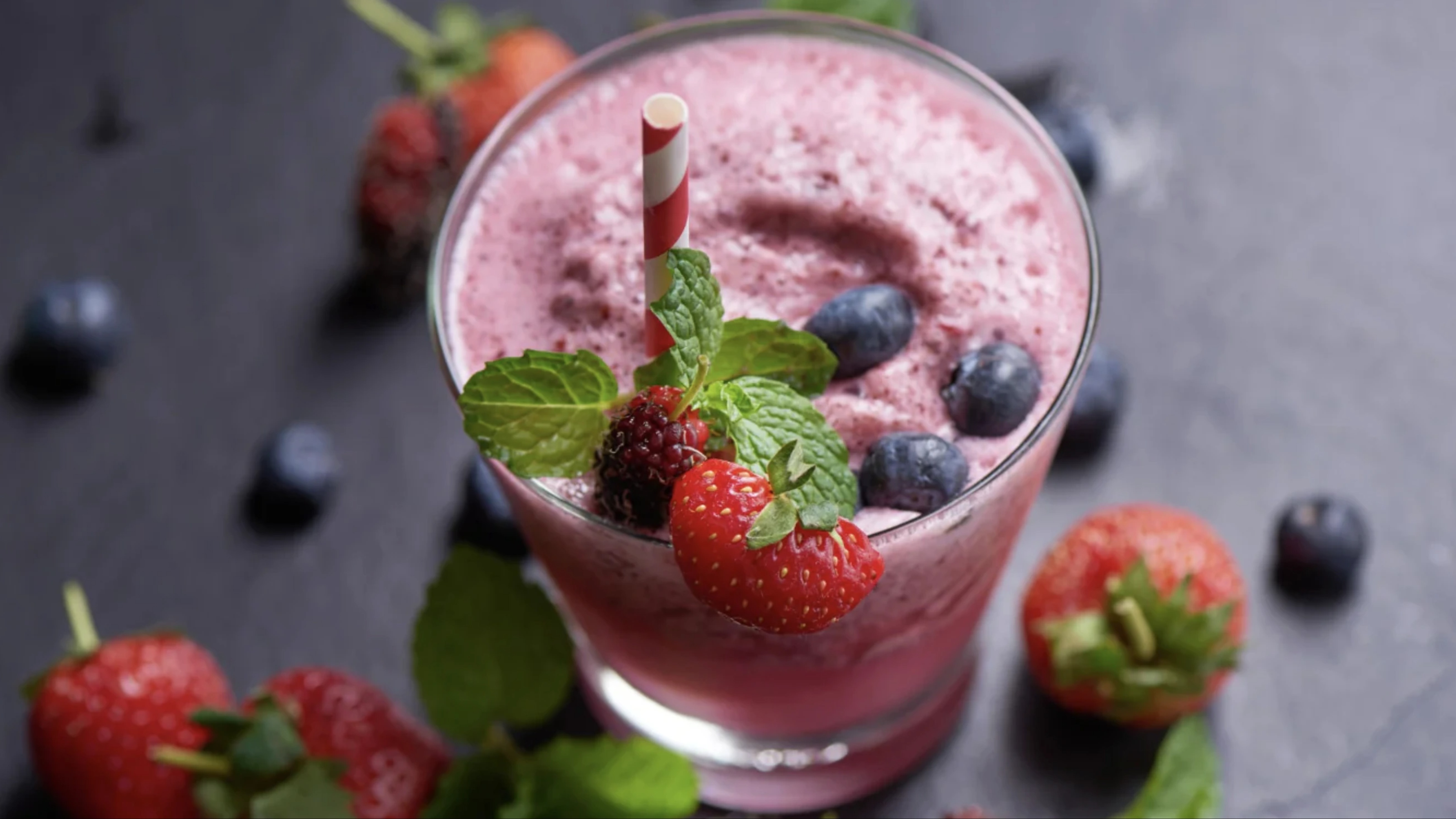 Vaso de batido de frutas con creatina magrolabs sobre una mesa junto a frutas frescas